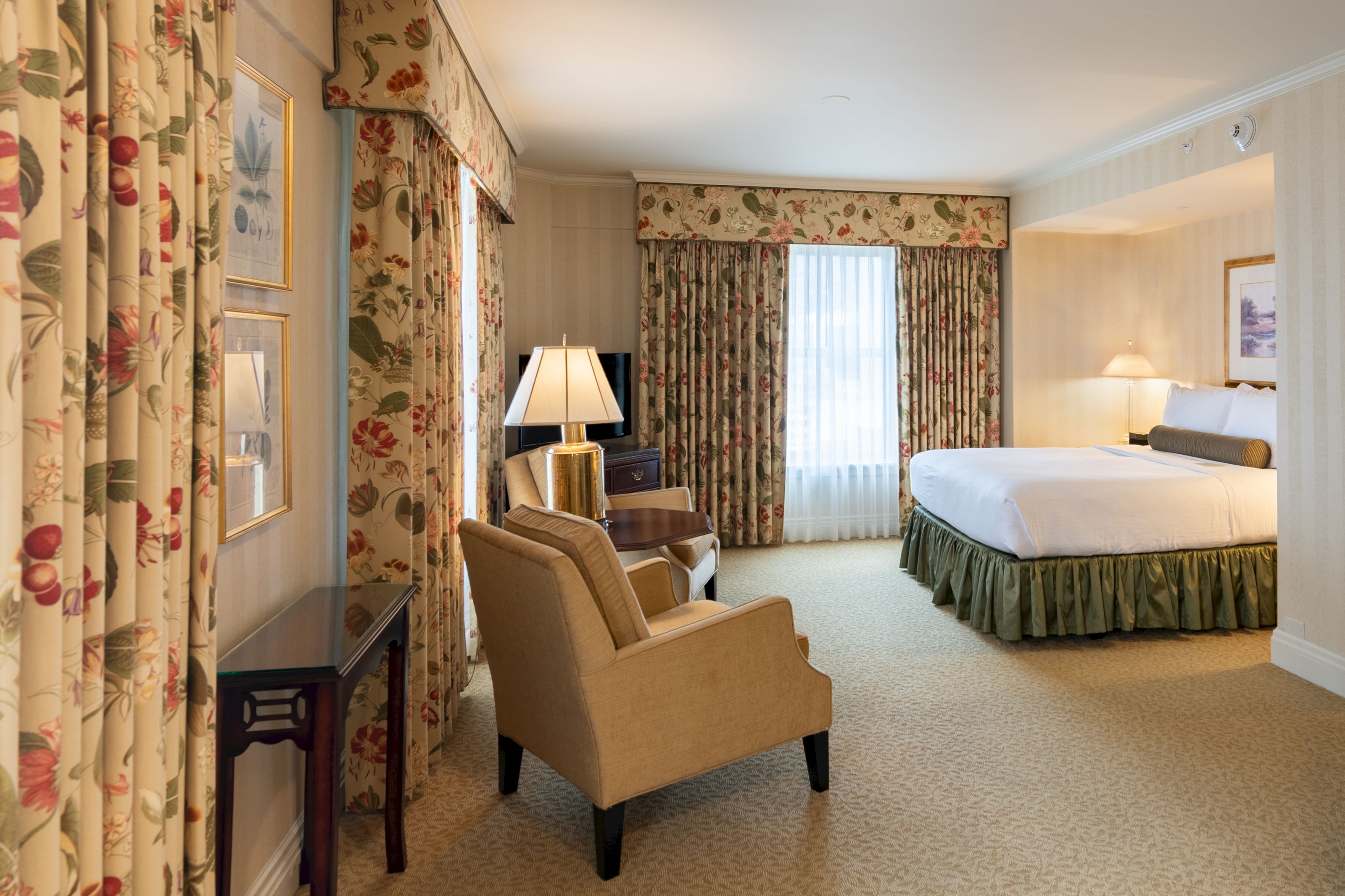 A wide view of a hotel room with a king-sized bed, floral curtains, and a desk area.