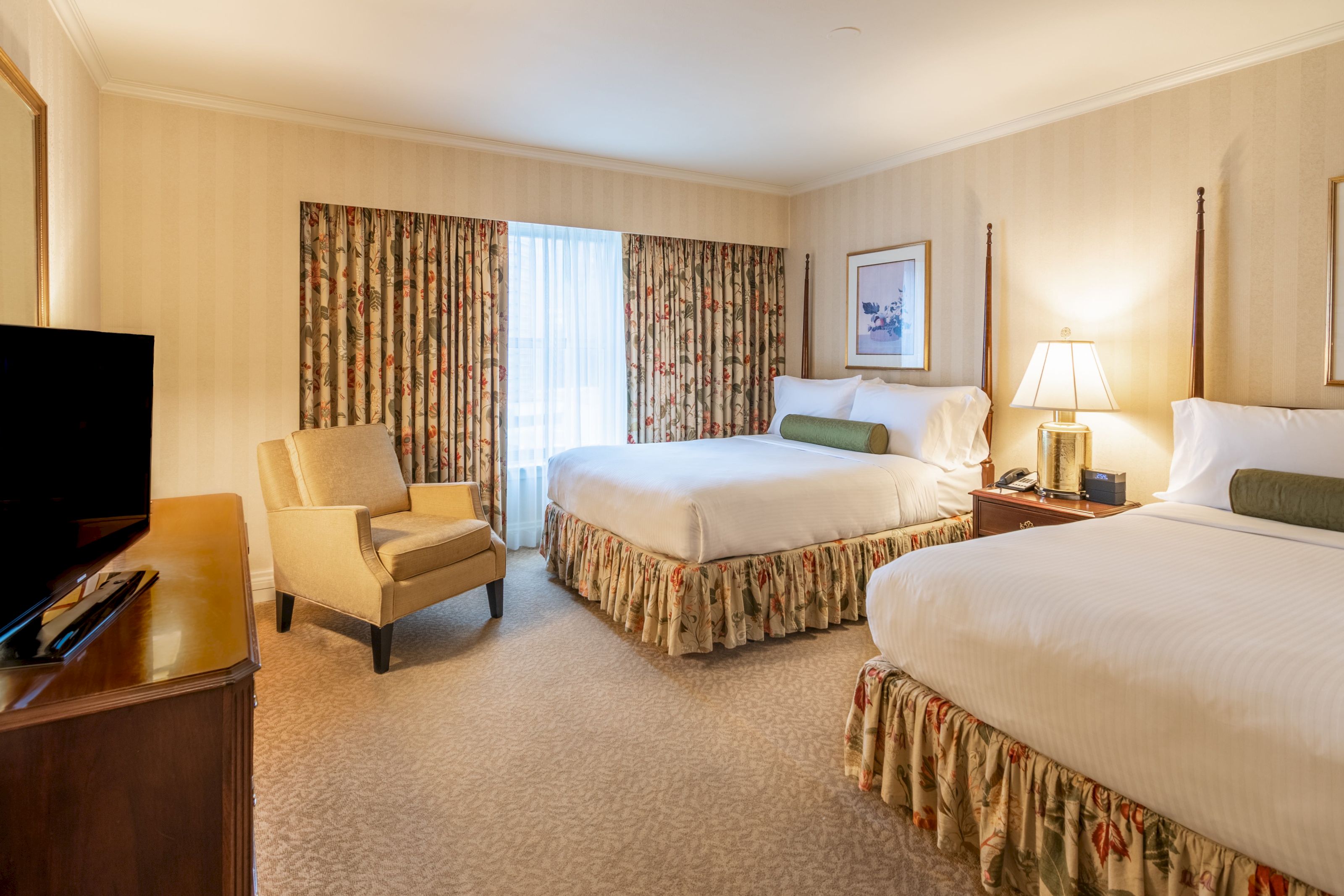 A hotel room with two beds, a flat-screen TV, a chair, and a window.
